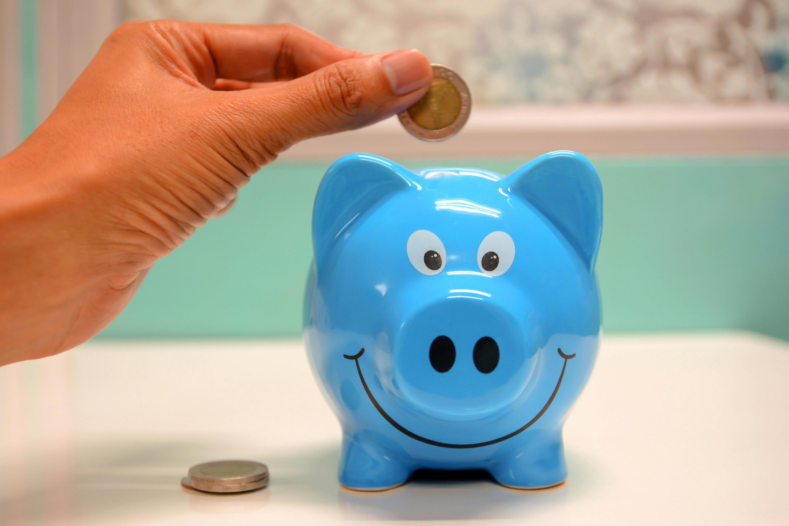 A hand putting money into a blue piggy bank